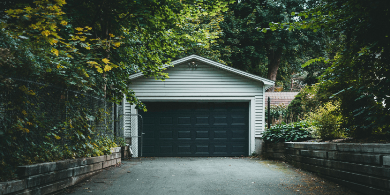 Green and white detached garage structure surrounded by trees and set back from the main villa